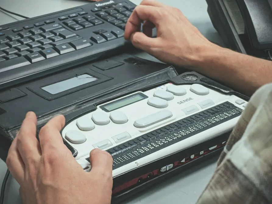 Le mani di una persona usano un display braille collegato sotto la tastiera di un computer