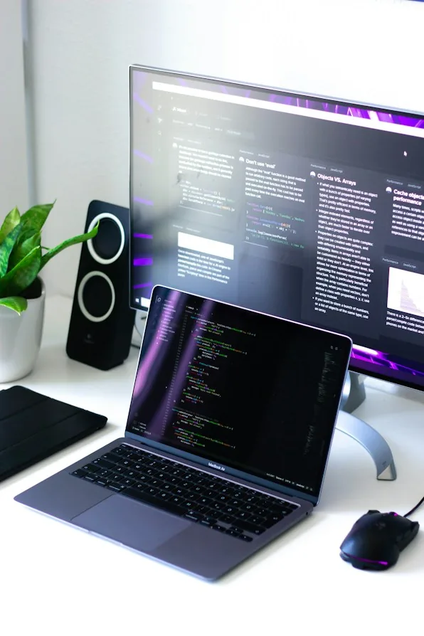 Un portatile aperto con del codice sullo schermo, accanto a un monitor e a una cassa
