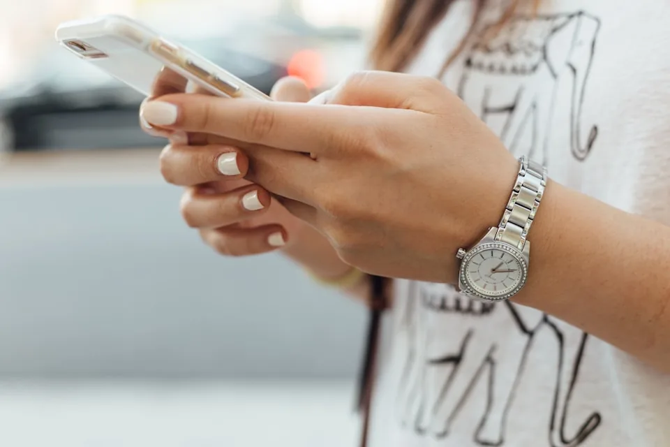 Le mani di una donna con un orologio da polso scrivono un messaggio sullo smartphone