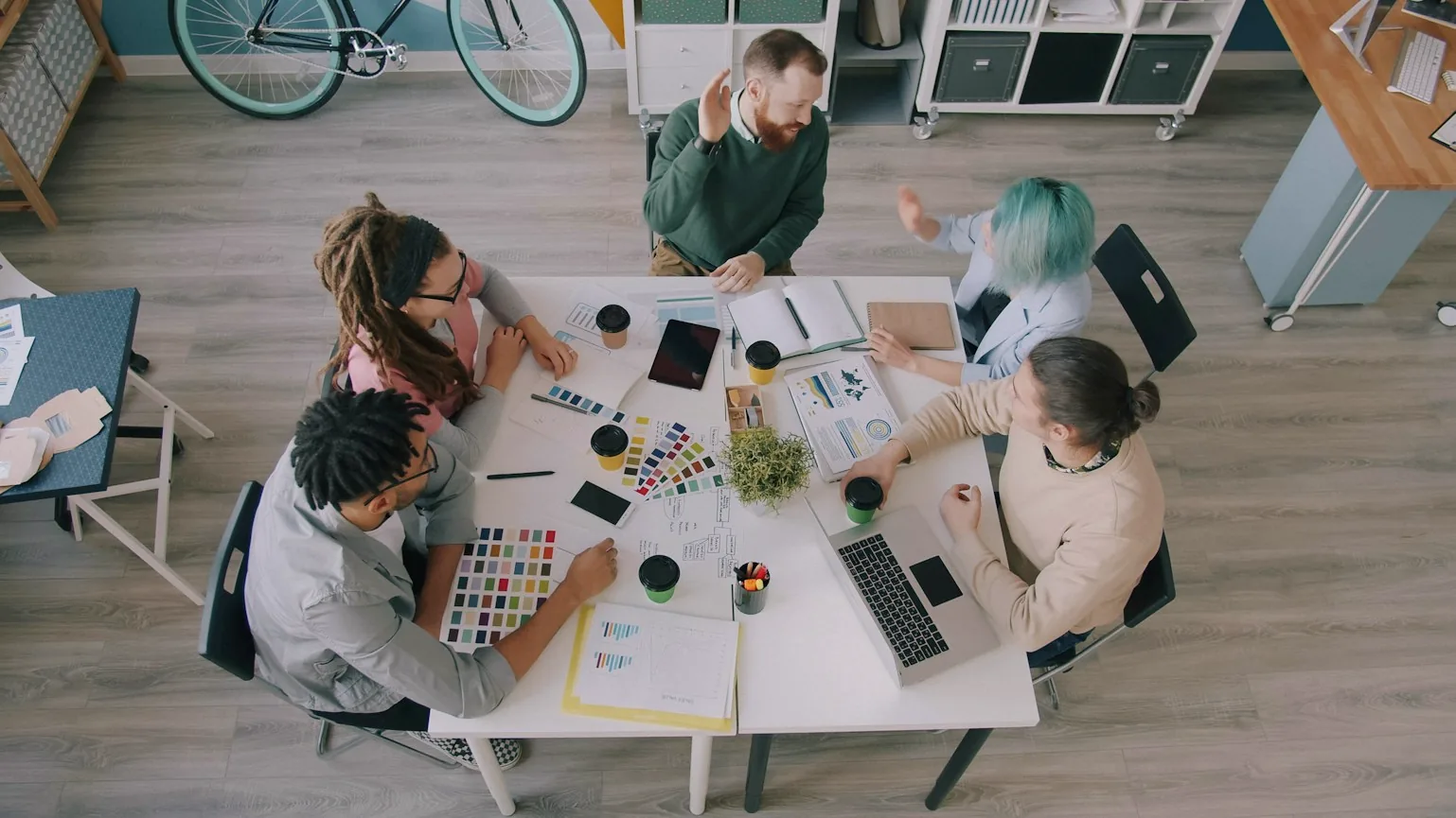 Vista dall’alto di un gruppo di persone al lavoro intorno a un tavolo con portatili, fogli e campioni di colore